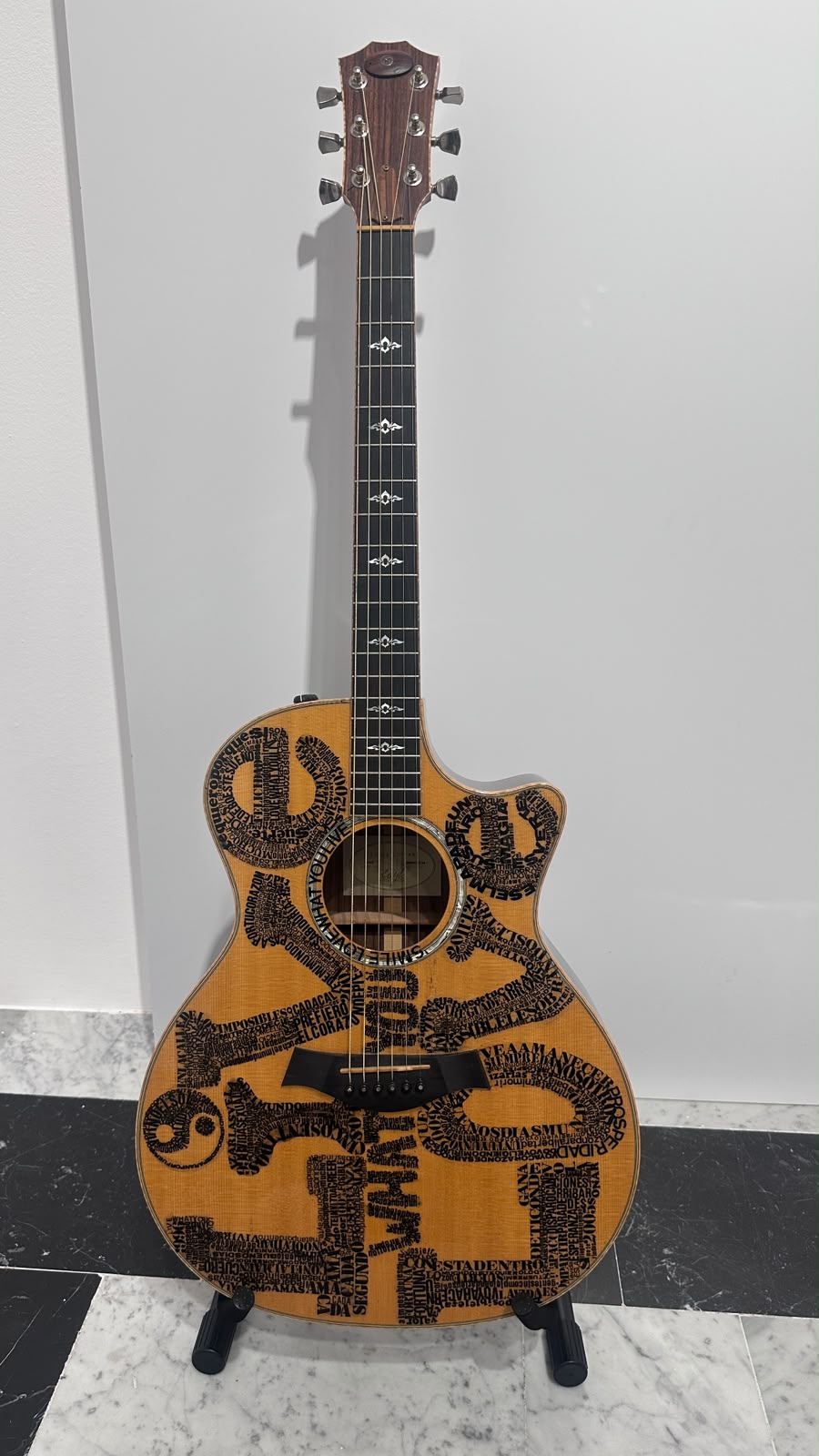 Vista completa de la guitarra decorada con letras, apoyada en su soporte